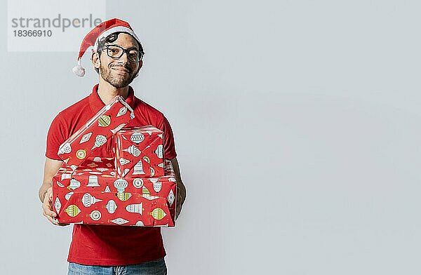 Weihnachten Mann Porträt hält Geschenk-Boxen und lächelnd isoliert. Lächelnder Mann mit Weihnachtsmannmütze  der Weihnachtsgeschenkboxen hält. Freundlicher Mann in weihnachtlicher Kleidung hält Geschenkboxen isoliert
