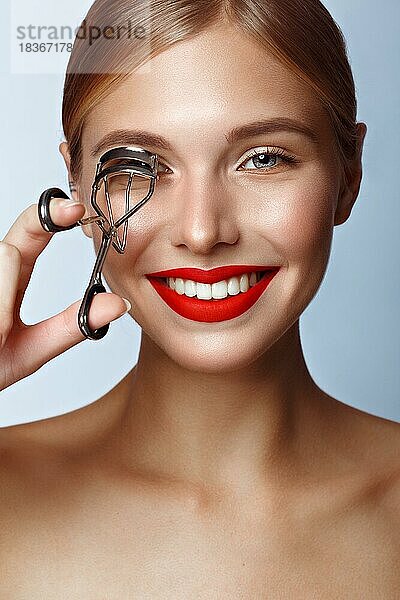 Schönes Mädchen mit roten Lippen und klassischem Make-up mit Lockenwickler in der Hand. Schönes Gesicht. Foto im Studio aufgenommen