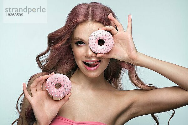 Schöne Frau mit rosa Haaren  schöne Make-up mit Donuts in ihren Händen posiert im Studio. Schönheit Gesicht und Haar