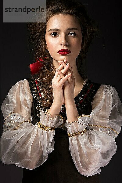 Schönes russisches Mädchen im Nationalkleid mit Zopffrisur und roten Lippen. Schönes Gesicht. Bild im Studio auf einem schwarzen Hintergrund genommen