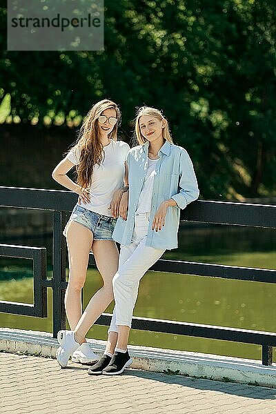 Zwei fröhliche Studentinnen stehen auf der Brücke an einem heißen sonnigen Tag