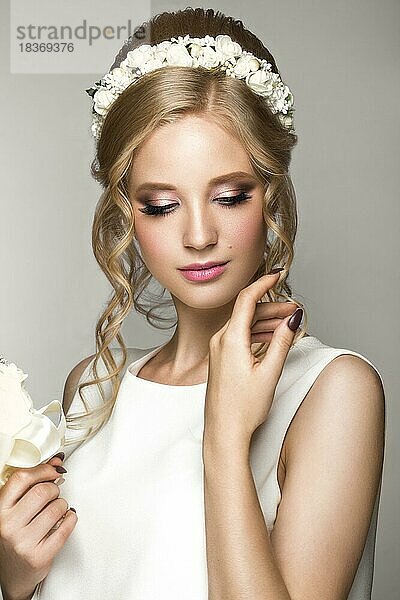 Porträt eines schönen blonden Mädchens im Bild der Braut mit weißen Blumen auf dem Kopf. Schönheit Gesicht. Foto im Studio auf einem grauen Hintergrund geschossen