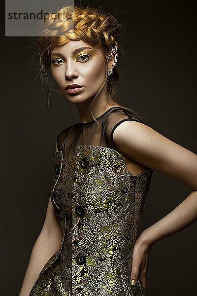 Schönes Mädchen in einem goldenen Kleid mit kreativem Make-up und Zöpfen auf dem Kopf. Die Schönheit des Gesichts. Fotos im Studio geschossen