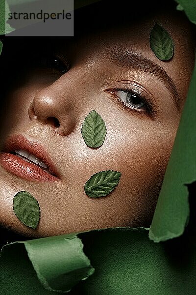 Schönes frisches Mädchen mit perfekter Haut  natürlichem Make-up und grünen Blättern. Schönes Gesicht. Foto im Studio aufgenommen