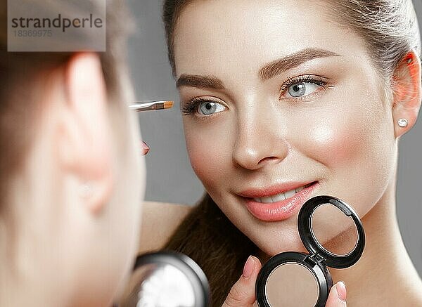 Schönes Mädchen macht sich ein Make-up in den Spiegel. Schönes Gesicht. Foto im Studio aufgenommen