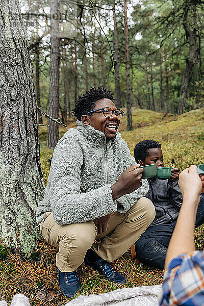 Glücklicher Vater hält Tasse  während er mit seiner Familie im Wald hockt