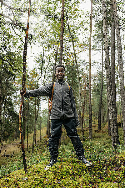 Porträt eines lächelnden Jungen mit Stock im Wald während der Ferien