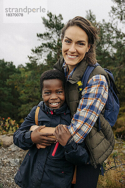 Porträt einer glücklichen Mutter  die ihren Sohn umarmt  während sie im Wald steht