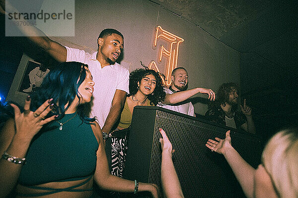 Fröhliche junge multirassische Männer und Frauen tanzen um einen DJ in einem beleuchteten Nachtclub