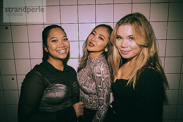 Porträt von lächelnden jungen multirassischen Freundinnen vor einer weißen Wand in einem Nachtclub