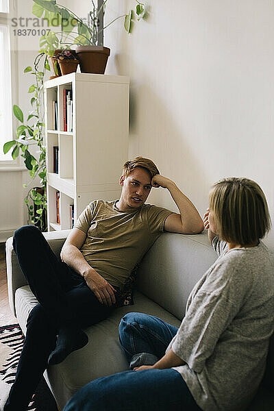 Mann im Gespräch mit einem Elternteil  während er zu Hause auf dem Sofa sitzt