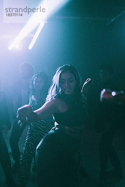 Junge Frau tanzt in einem Nachtclub gegen Freunde im Hintergrund