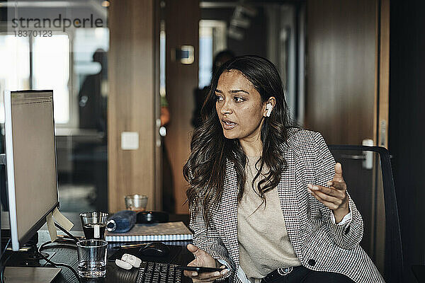 Unternehmerin schaut auf den Computer  während sie im Büro mit ihrem Smartphone spricht