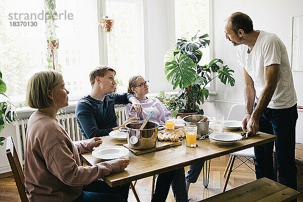 Familie im Gespräch mit Vater  der zu Hause am Tisch steht