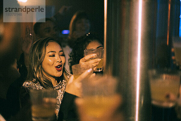 Glückliche junge Frau mit einem Getränk in der Hand  die mit Freunden in einem Nachtclub tanzt