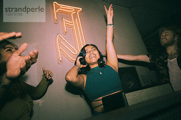 Fröhlicher junger weiblicher DJ tanzt inmitten von Freunden und genießt das Wochenende in einem Nachtclub