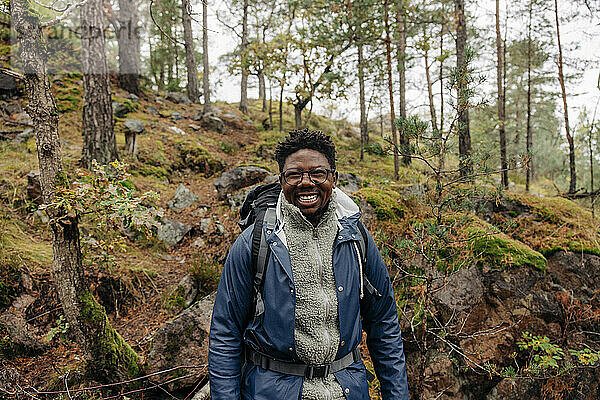 Glücklicher reifer Mann mit Rucksack im Wald stehend im Urlaub