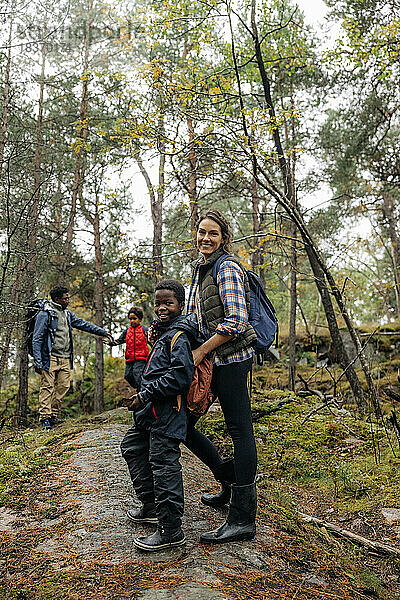 Seitenansicht einer lächelnden Frau  die mit ihrem Sohn auf einem Wanderweg im Wald steht