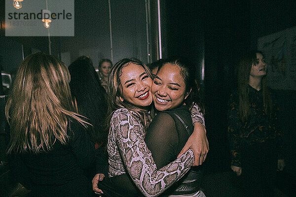 Porträt von fröhlichen jungen Frauen  die sich umarmen  während sie sich in einem Nachtclub vergnügen