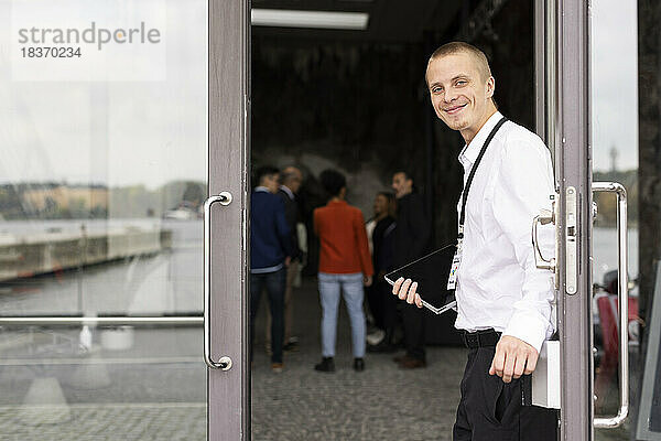 Porträt eines lächelnden jungen Geschäftsmannes  der am Eingang eines Kongresszentrums steht
