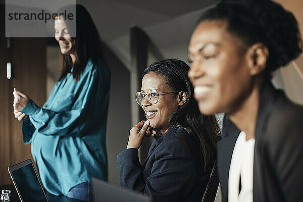 Lächelnde Geschäftsfrau mit Hand am Kinn von Kollegen während einer Besprechung im Büro