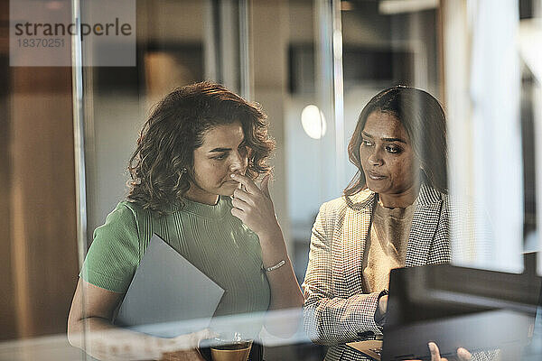 Geschäftsfrau schaut auf den Laptop  den eine Kollegin im Büro hält