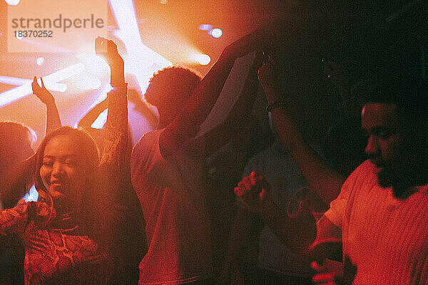 Glückliche junge männliche und weibliche Freunde genießen den Tanz in einem beleuchteten roten Nachtclub