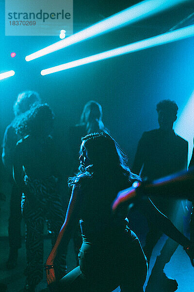 Rückansicht einer jungen Frau  die in der Nähe von Freunden auf der Tanzfläche eines Nachtclubs tanzt