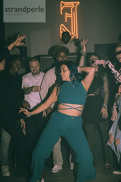 Junge Frau tanzt in einem Nachtclub gegen ihre multirassischen Freunde