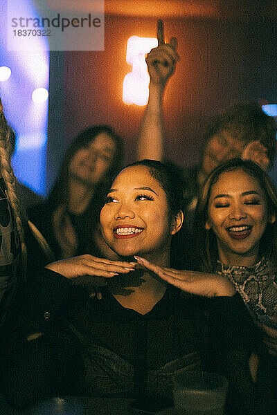 Glückliche junge Frau genießt beim Tanzen mit Freunden im Club in der Nacht während des Wochenendes