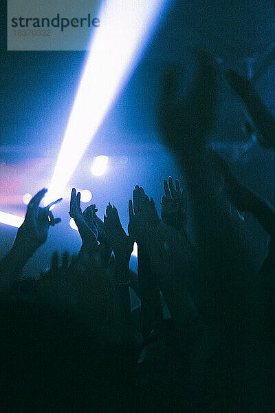 Silhouette erhobener Hände von Frauen und Männern  die in einem Nachtclub tanzen