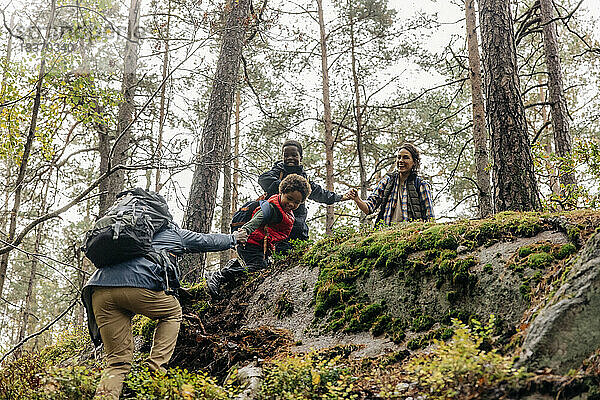 Familie hilft Vater beim Klettern während einer Wanderung im Wald