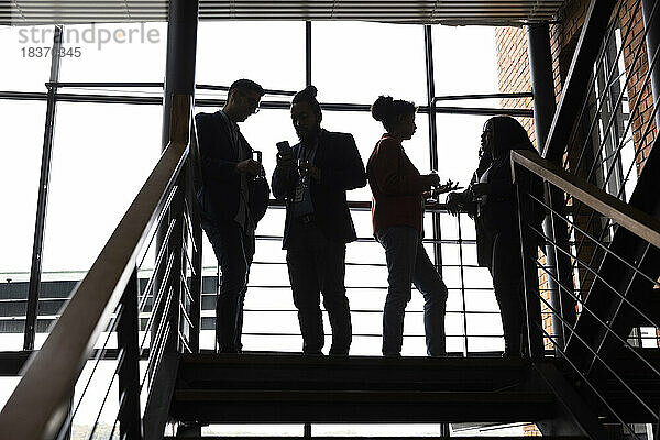 Multirassische männliche und weibliche Unternehmer diskutieren miteinander auf einer Treppe bei einer Firmenveranstaltung