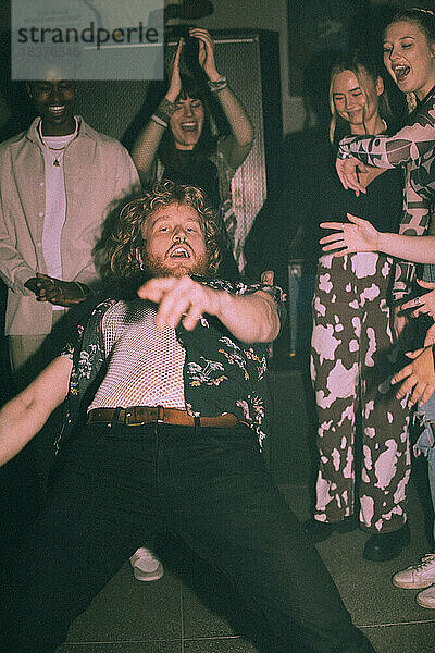 Porträt eines biegsamen jungen Mannes  der sich nach hinten beugt und inmitten von Freunden in einem Nachtklub tanzt