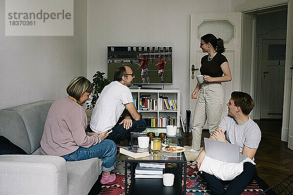 Familie im Gespräch mit der Tochter  während sie zu Hause im Wohnzimmer Fußball im Fernsehen sieht