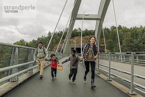 Glückliche Familie hält sich an den Händen  während sie im Urlaub auf einer Brücke läuft