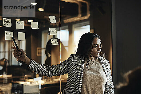 Geschäftsfrau zeigt auf Klebezettel an der Wand während einer Besprechung im Büro