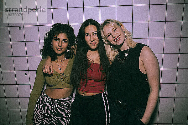 Porträt junger multirassischer Freundinnen  die mit den Armen an der weißen Wand eines Nachtclubs stehen