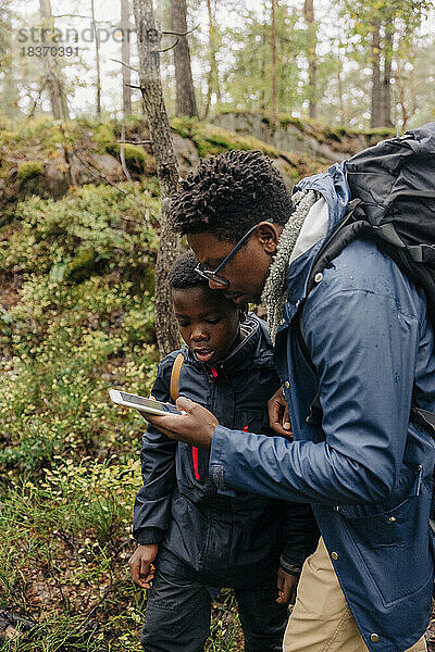 Vater benutzt Smartphone mit Sohn bei der Erkundung des Waldes im Urlaub