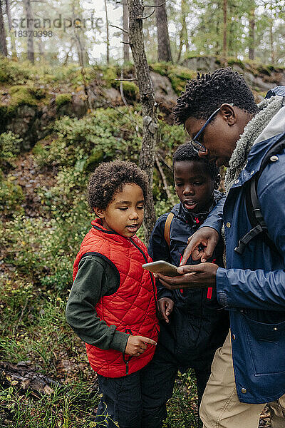 Vater zeigt seinen Söhnen beim Wandern im Wald das Smartphone