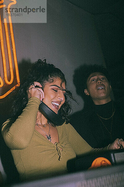Fröhlicher junger weiblicher DJ mit Kopfhörern an einem Freund  der in einem Nachtclub tanzt