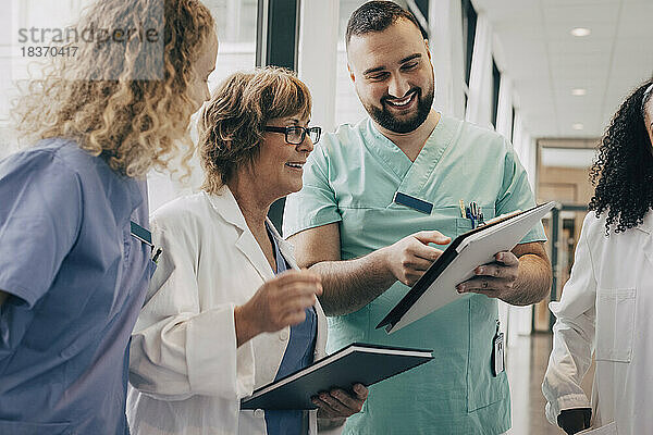 Lächelndes multirassisches Ärzteteam bespricht sich über einem Klemmbrett im Krankenhaus