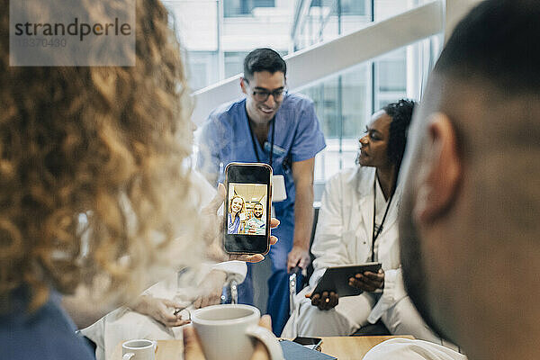 Weibliche Krankenschwester  die während einer Kaffeepause im Krankenhaus ein Selfie mit einem Kollegen per Smartphone macht