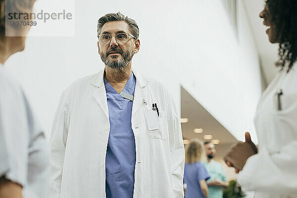 Reifer männlicher Arzt im Laborkittel diskutiert mit Kollegen im Krankenhaus