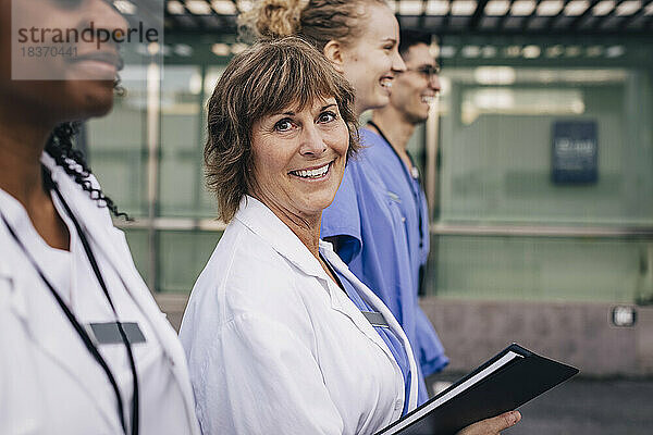 Porträt einer Ärztin mit einer Akte in der Hand von Krankenhauskollegen