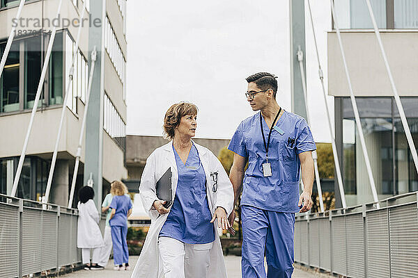 Männlicher Mitarbeiter im Gesundheitswesen im Gespräch mit einer Ärztin auf einer Brücke
