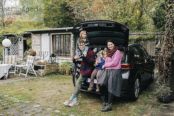 Glückliche Eltern mit Töchtern in der Nähe des vor dem Haus geparkten Elektroautos