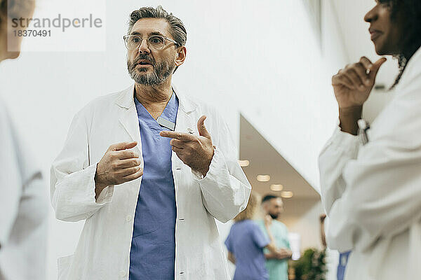 Männlicher Arzt gestikuliert während einer Diskussion mit Kollegen im Krankenhaus