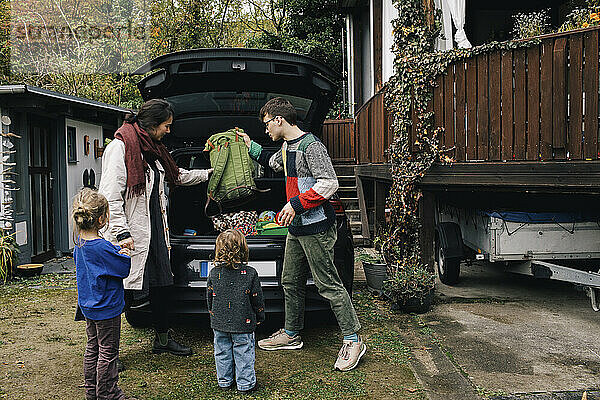 Familie bereitet sich auf ein Picknick vor  während sie Sachen in den Kofferraum eines Elektroautos lädt