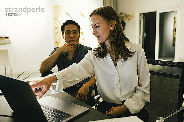 Geschäftsfrau  die mit einem männlichen Kollegen über einen Laptop diskutiert  während sie im Büro sitzt